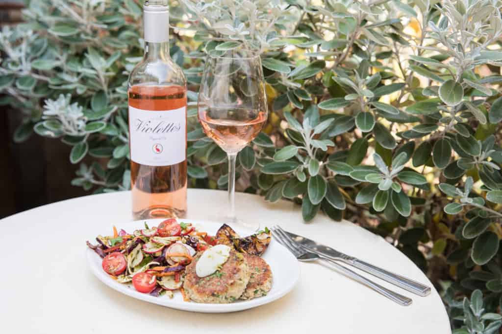 An outdoor table with a bottle of rosé, a glass and a plated dish