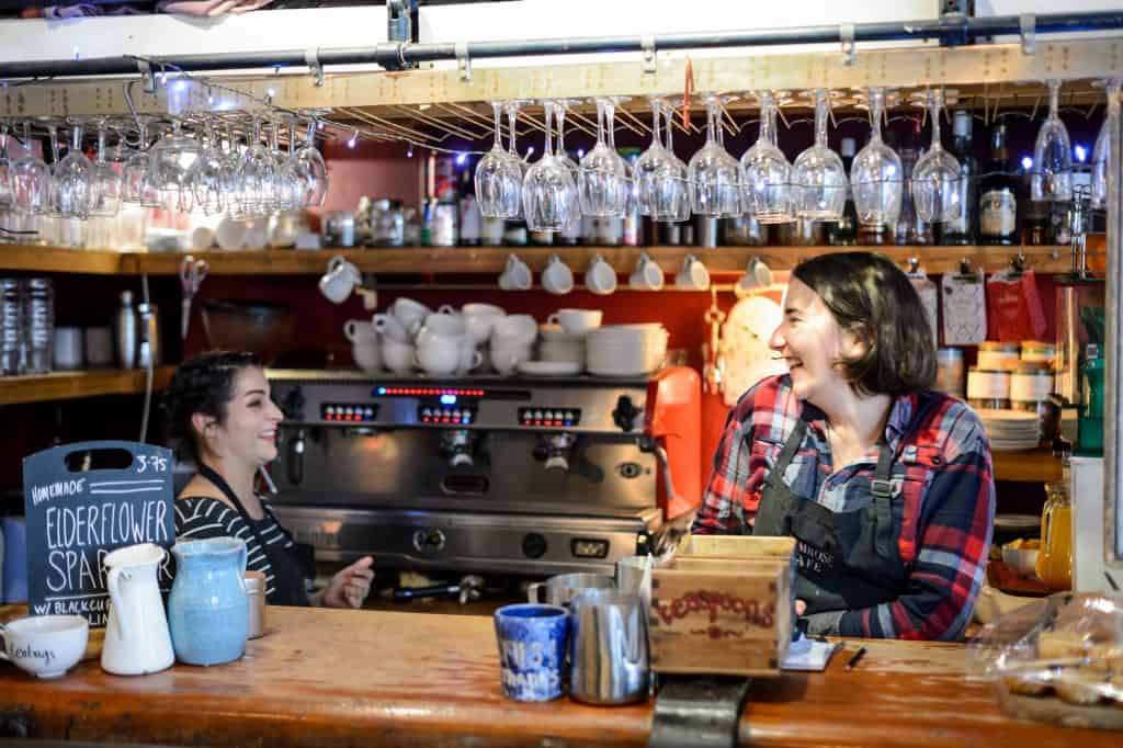Inside Primrose Cafe: the counter and coffee machine, with staff at work in warm light